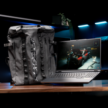 Load image into Gallery viewer, AFTERSHOCK APEX 16R laptop open at a slight angle showing keyboard and game on-screen next to a black Aftershock branded.